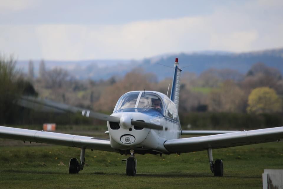 G-ATON viewed head-on on the grass, with wooded hills behind